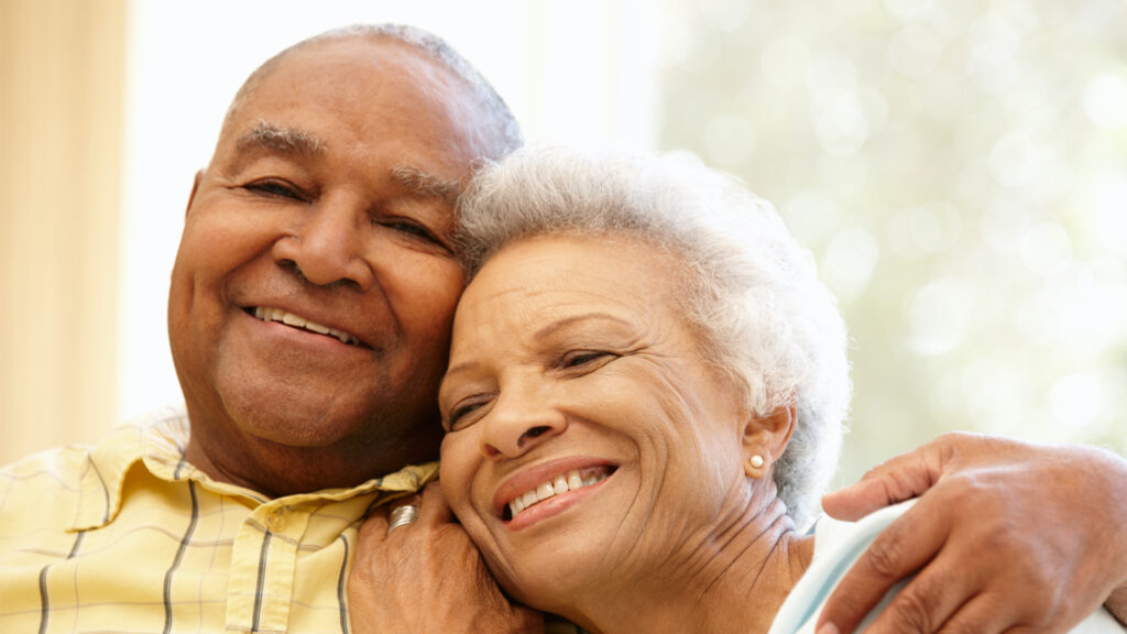 Elderly couple smiling and embracing warmly.